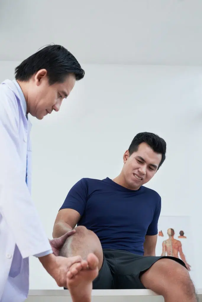 Doctor examining patient suffering from severe pain in his knee and leg
