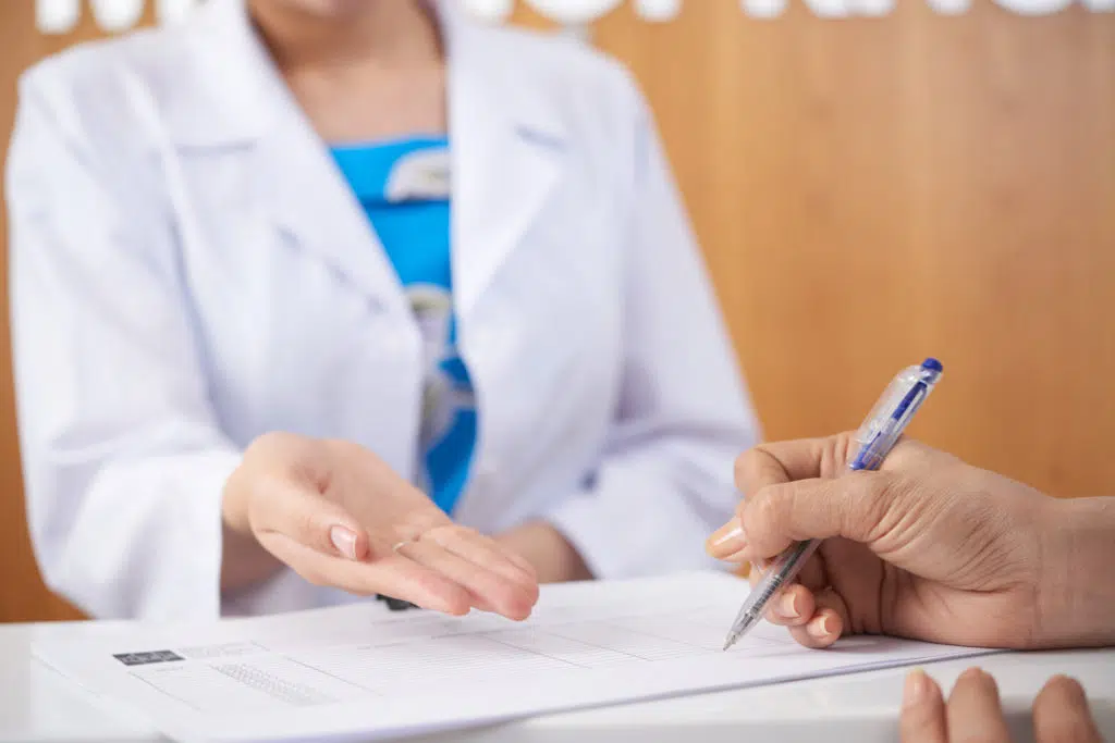 chiropractor's hand over an insurance document being signed by a patient