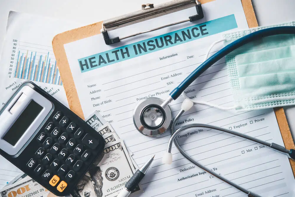 Health insurance paper form with a calculator, stethoscope, money, mask, & pen on the table