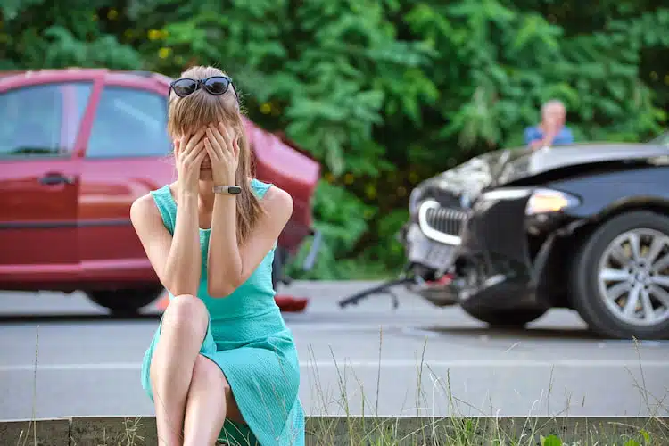 Stressed woman driver sitting on street sidelooking shocked after a car accident