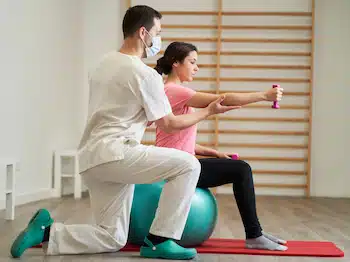 physiotherapist doing rehabilitation exercises with the patient with a gym ball and light-weight dumbells